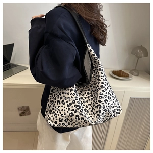 Close-up of a large leopard print tote bag worn on shoulder by a model in a cozy room