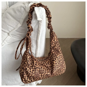 Close-up of leopard print canvas crescent bag with ruched shoulder strap on sofa
