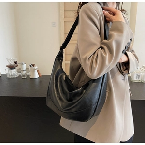 Detailed view of a black slouchy half-moon hobo bag styled with a beige blazer