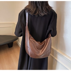 Detail of a brown vintage leather crescent tote bag worn over a black blazer