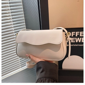 Detail shot of the wave-edged flap and golden metal hardware on the white shoulder bag