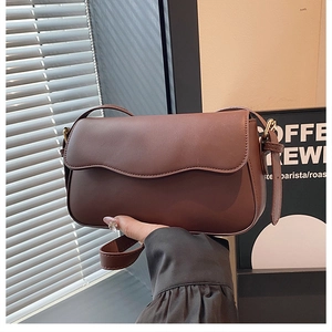 Detail of dark brown leather shoulder bag featuring a unique wavy flap and metal buckle