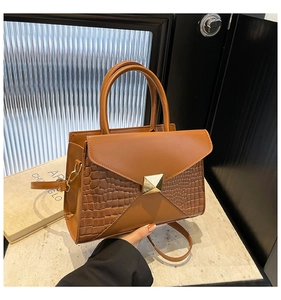 Detail of brown faux leather handbag with crocodile pattern panels and gold metal clasp