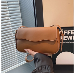 Close-up of caramel brown handbag featuring unique wavy flap design and magnetic closure