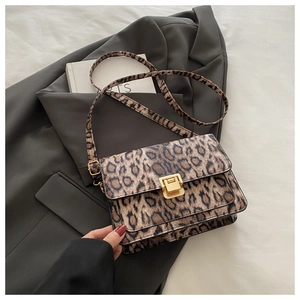 Detailed view of leopard print crossbody bag with gold square buckle on a grey suit jacket