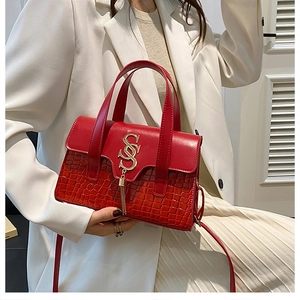 Detail of red crossbody bag featuring crocodile texture and golden tassel hardware