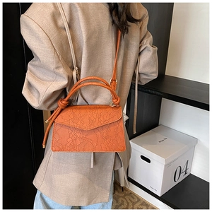 Detail of orange lace embossed texture crossbody bag with unique knotted top handle