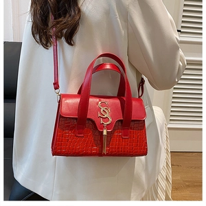 Side view of woman in white suit wearing red croc-embossed handbag with gold tassel detail