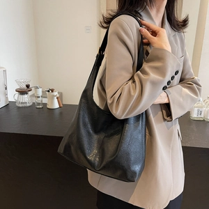 Retro black oversized hobo shoulder bag in textured leather worn by a model in a cafe