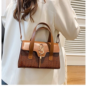 Detail of a brown crocodile texture bag featuring gold logo and decorative tassel
