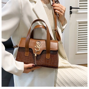Detail of brown leather handbag with crocodile pattern and golden S-shaped hardware