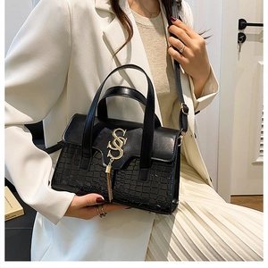 Woman in white suit carrying a black crocodile-embossed leather tote bag with gold hardware