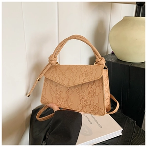 Close-up of apricot lace-textured embossed handbag with decorative knotted handle detail