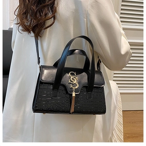 Macro shot of luxury black handbag featuring crocodile texture and golden tassel hardware