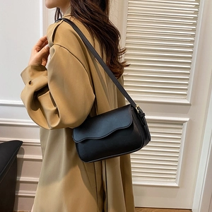 Minimalist black leather shoulder bag with wavy flap design shown on model