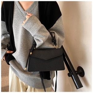 Détail du sac à main noir tressé avec poignée nouée et anneaux en métal doré