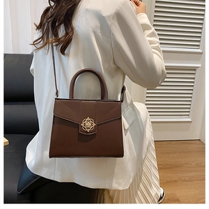 Detail of elegant dark brown shoulder bag with golden clover clasp and crossbody strap