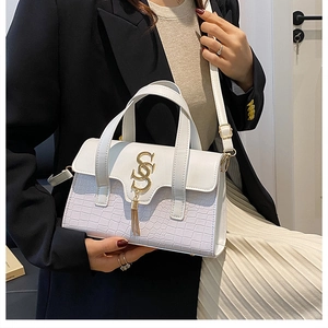 Detail view of white crocodile pattern handbag with gold logo and tassel on a model