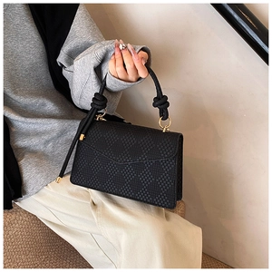 Détail d'un sac à main noir tressé avec poignée à nœud et garnitures dorées élégantes