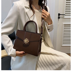 Detail of elegant caramel handbag featuring a golden floral clasp and refined top handle