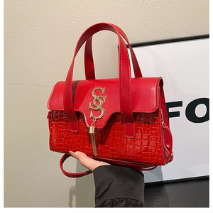 Detailed view of red handbag featuring croc-embossed texture and gold metal logo tassel