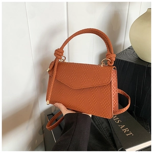 Détail d'un sac à main marron à texture tressée avec nœuds et anneaux dorés
