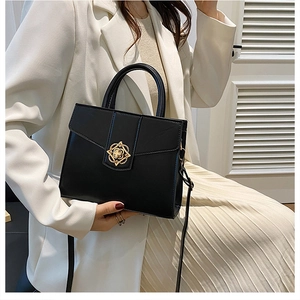 Close-up of black leather handbag with gold flower lock on a model in white blazer
