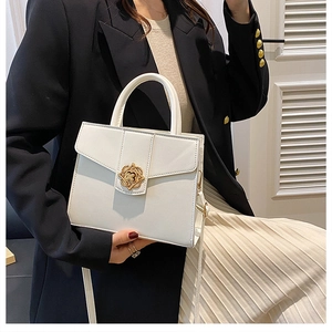 Close-up of white minimalist shoulder bag with golden clover metal clasp and top handle
