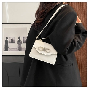 Detail of cream white leather handbag with sparkling rhinestone bow on model shoulder