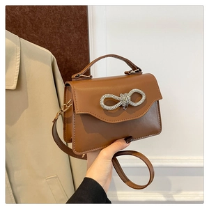 Close-up of brown PU leather bag with sparkling silver rhinestone bow and top handle