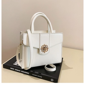 Detail of white structured handbag featuring a gold floral metal buckle on a dark book