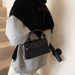 Sac bandoulière noir à texture tressée avec poignée nouée porté par un mannequin stylé