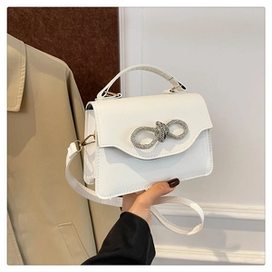 Close-up of sparkling rhinestone bow detail on a white leather handheld square bag