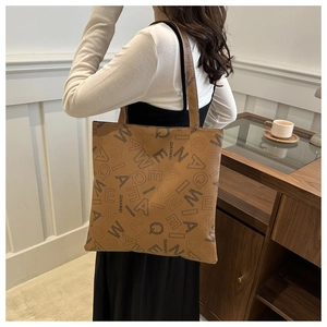 Detail view of large brown leather tote bag with letter print shown on a model