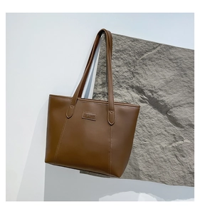 Detail view of brown leather tote bag with FASHION embossed label on textured stone