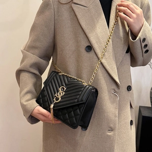 Sac bandoulière noir matelassé avec pompon doré et chaîne porté par un mannequin femme