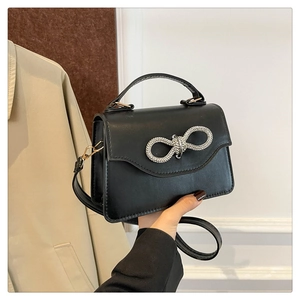 Detail of black leather handbag with sparkling crystal bow and gold hardware accents