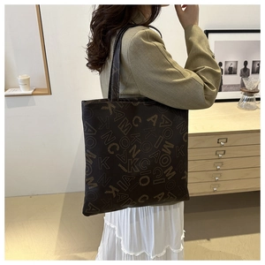 Detail of a large dark brown faux leather tote bag with gold letter prints on the shoulder