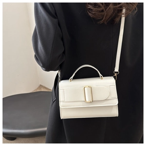 White minimalist square crossbody bag with gold buckle worn on a black suit jacket