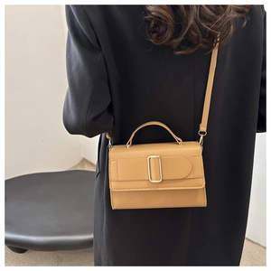 Detail of khaki leather shoulder bag with gold metal buckle shown on a black coat