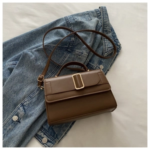 Detail of a brown PU leather crossbody bag with golden buckle on denim jacket background