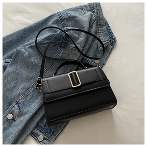 Close-up of a black crossbody bag with gold buckle on denim jacket and white bedding
