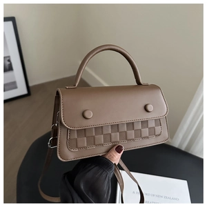 Detail of a brown crossbody bag with dual decorative rings and checkerboard texture