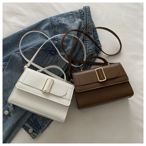 Close-up of minimalist white and dark brown crossbody bags with large gold square buckles