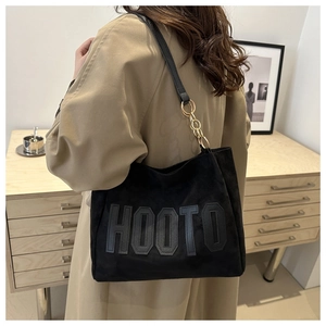 Detail of black suede tote bag with HOOTO lettering and gold chain on shoulder strap