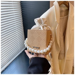Dettaglio della borsa a secchiello in paglia beige con fodera a coulisse e manico di perle