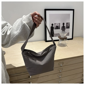 Detail of grey nylon shoulder bag with pleated texture held by model in modern home