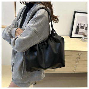 Detail of black pleated cloud tote bag in soft PU leather worn by model on shoulder