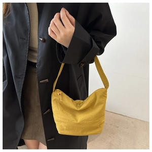 Close-up of mustard yellow nylon crescent bag on black coat with minimalist design