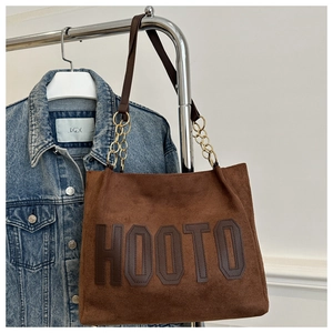 Dettaglio di una borsa tote in pelle scamosciata marrone con patch HOOTO e catena